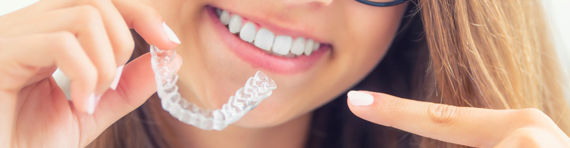 Girl pointing at clear aligner in her hand.